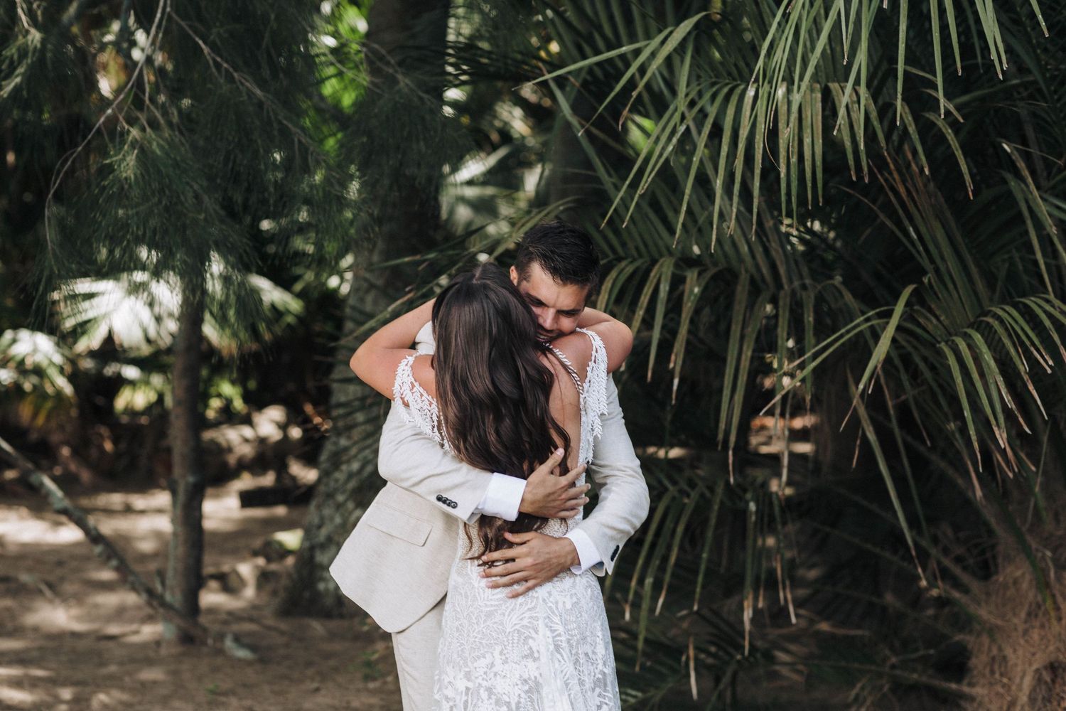 Couple embracing under tropical palm trees in romantic wedding photos.