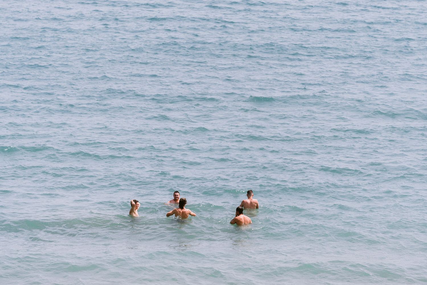 People swimming in crystal clear ocean waters near a tropical coastline on a sunny day.