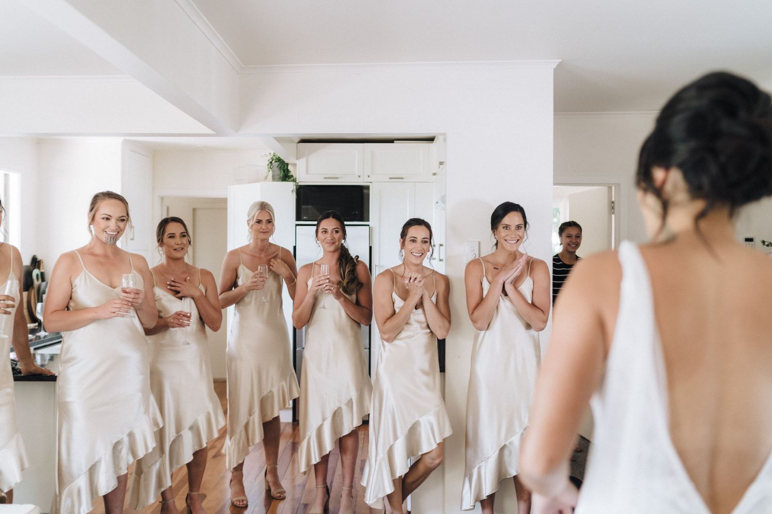Bridesmaids in champagne-colored dresses react emotionally during a pre-wedding moment.
