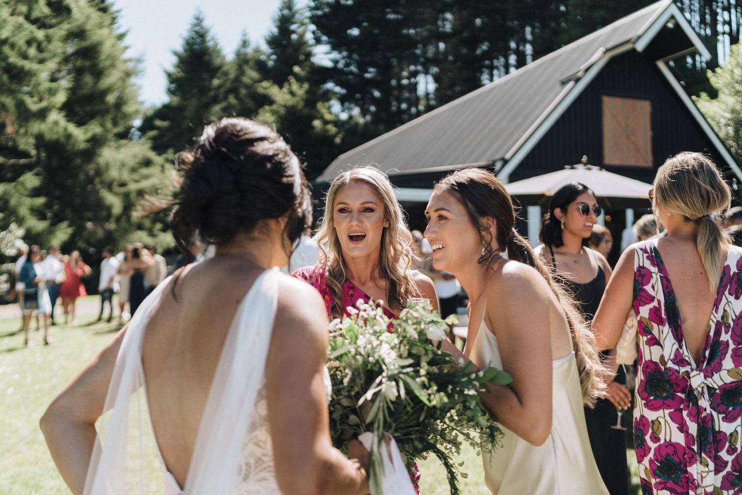 Wedding party members share joyful laughter while holding bouquets at an outdoor venue.