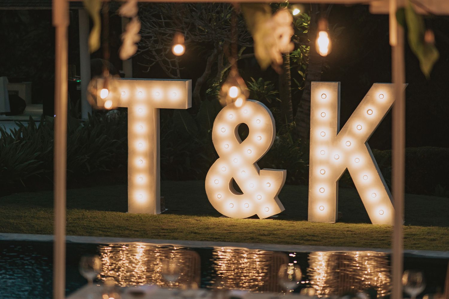 Illuminated T&K marquee letters glowing at night by pool.