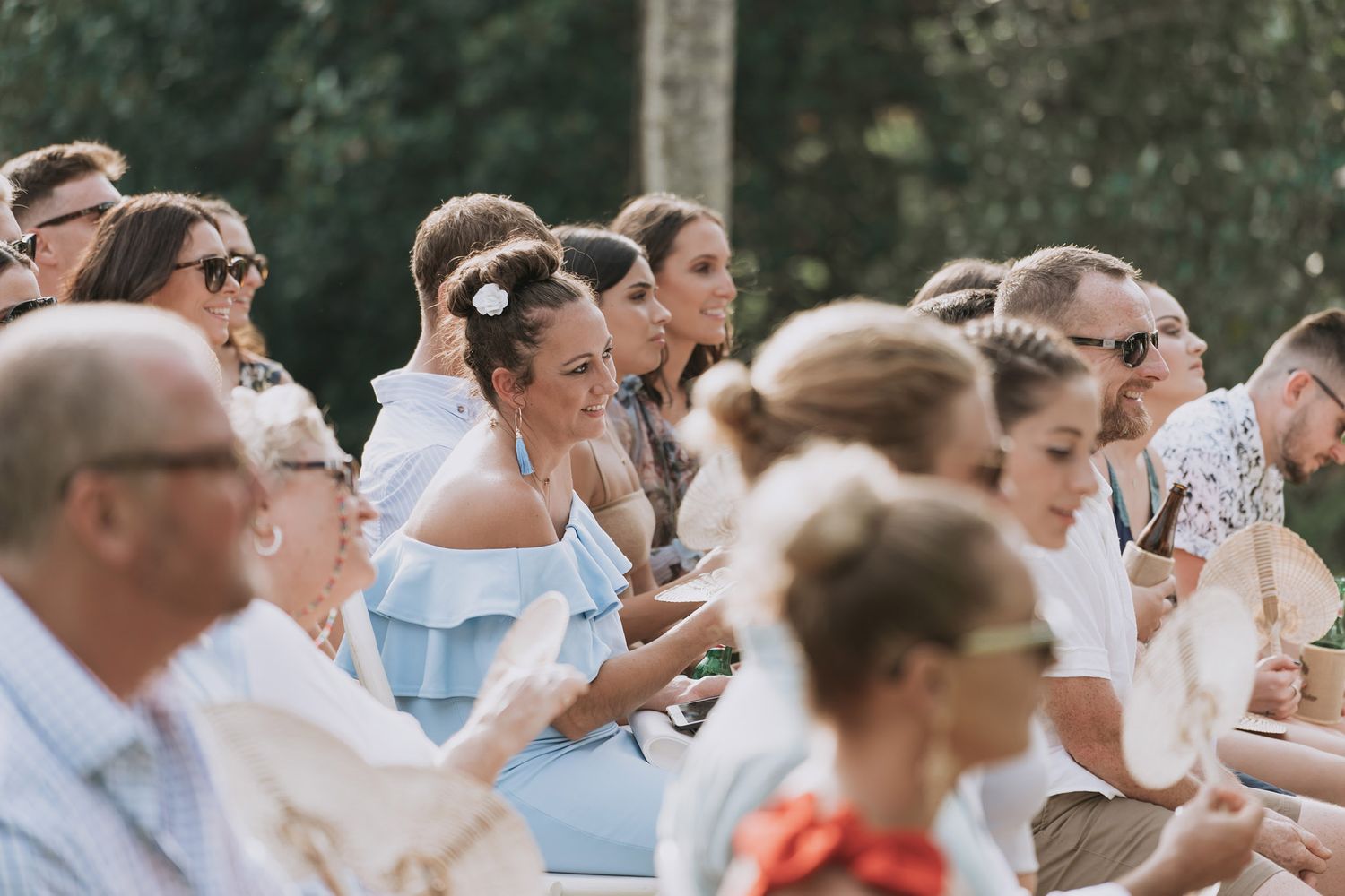 Wedding guests seated outdoors in summer attire watching ceremony.