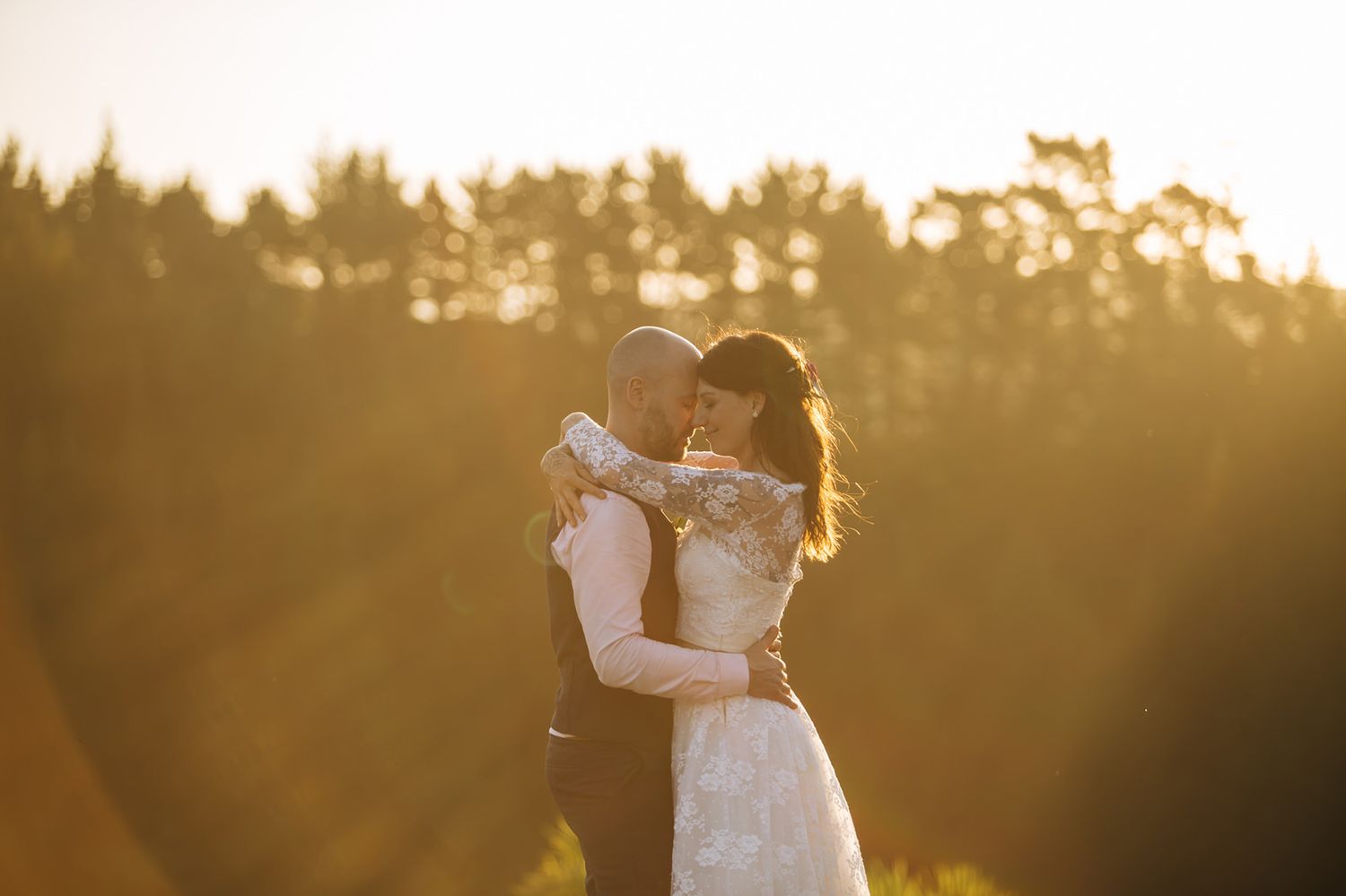 A couple embraces in a romantic sunset silhouette against a golden backlit forest background.
