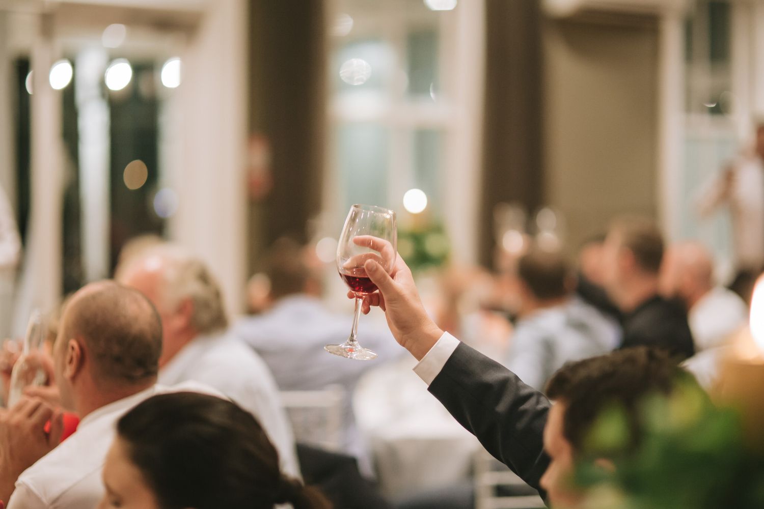Wedding guests raise their glasses in a toast during an elegant indoor reception celebration.