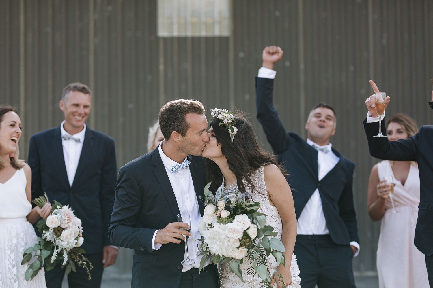 A romantic wedding celebration moment with joyful guests cheering in the background at a rustic barn venue.