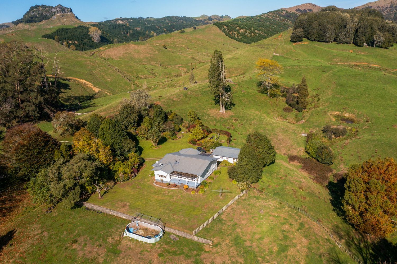 Aerial view of a white house nestled in rolling green hills surrounded by autumn trees.