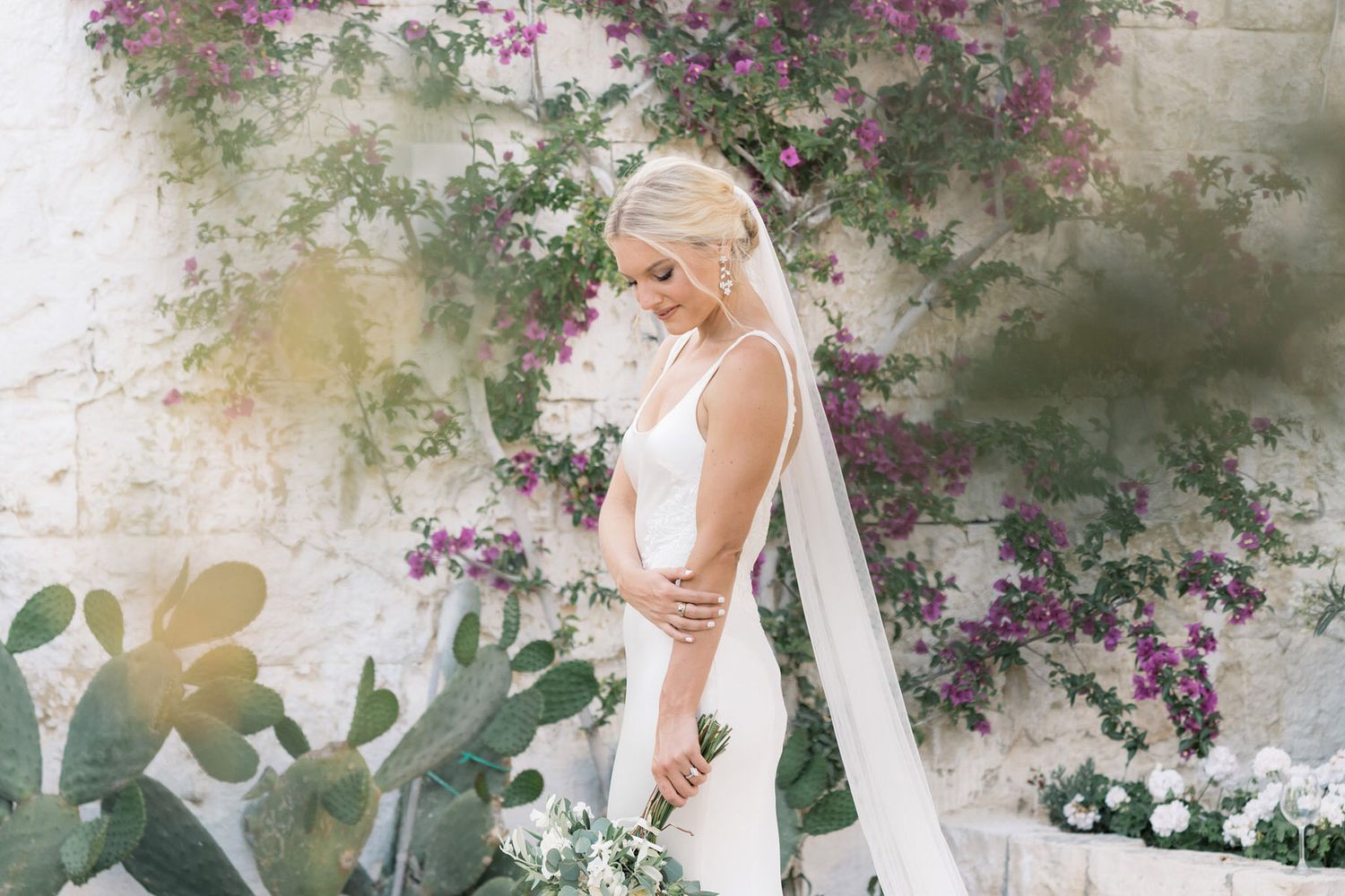 A couple shares an intimate moment in a romantic garden setting with climbing flowers and stone walls in soft light.