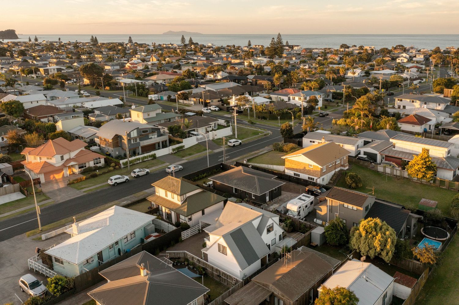Aerial panoramic view of residential neighborhoods in suburbia during golden sunset lighting over coastal town.