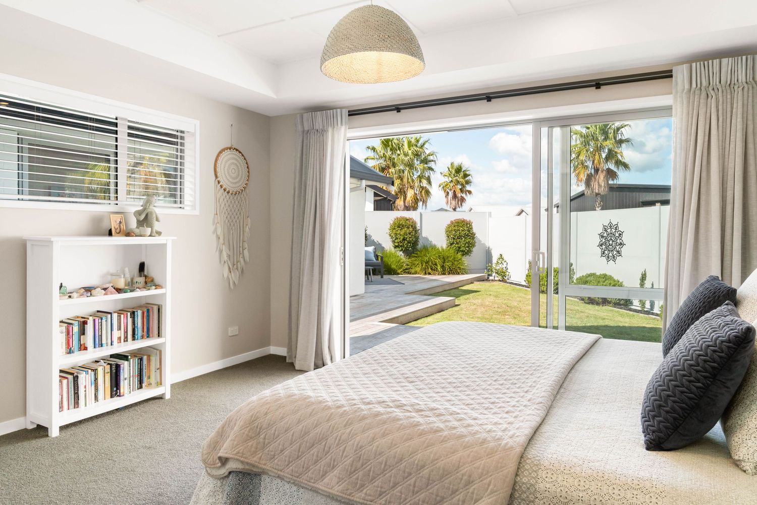 Bright modern bedroom with bookshelf and large sliding doors opening to garden view.