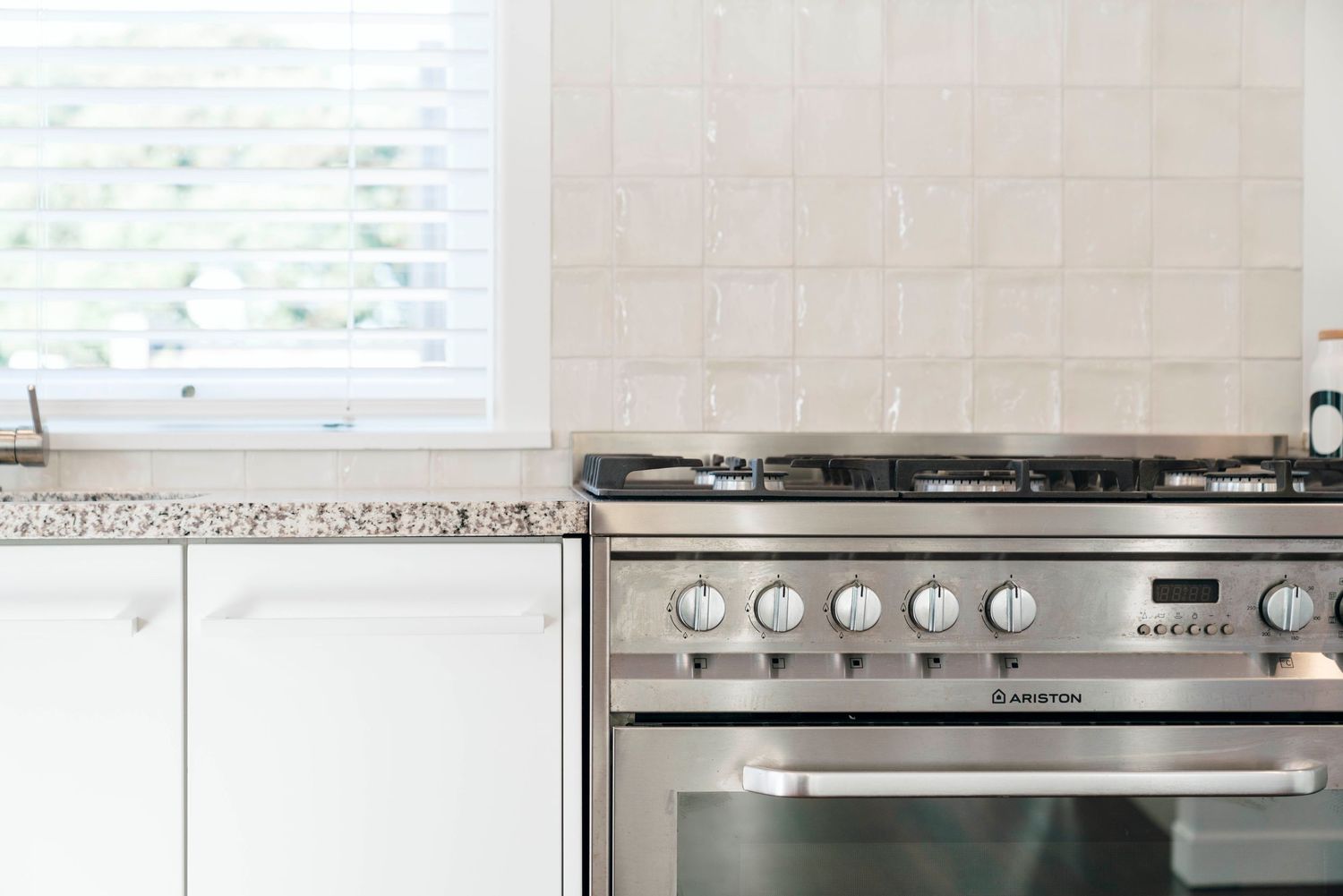 Modern white kitchen counter with stainless steel stove and granite countertop beneath window.