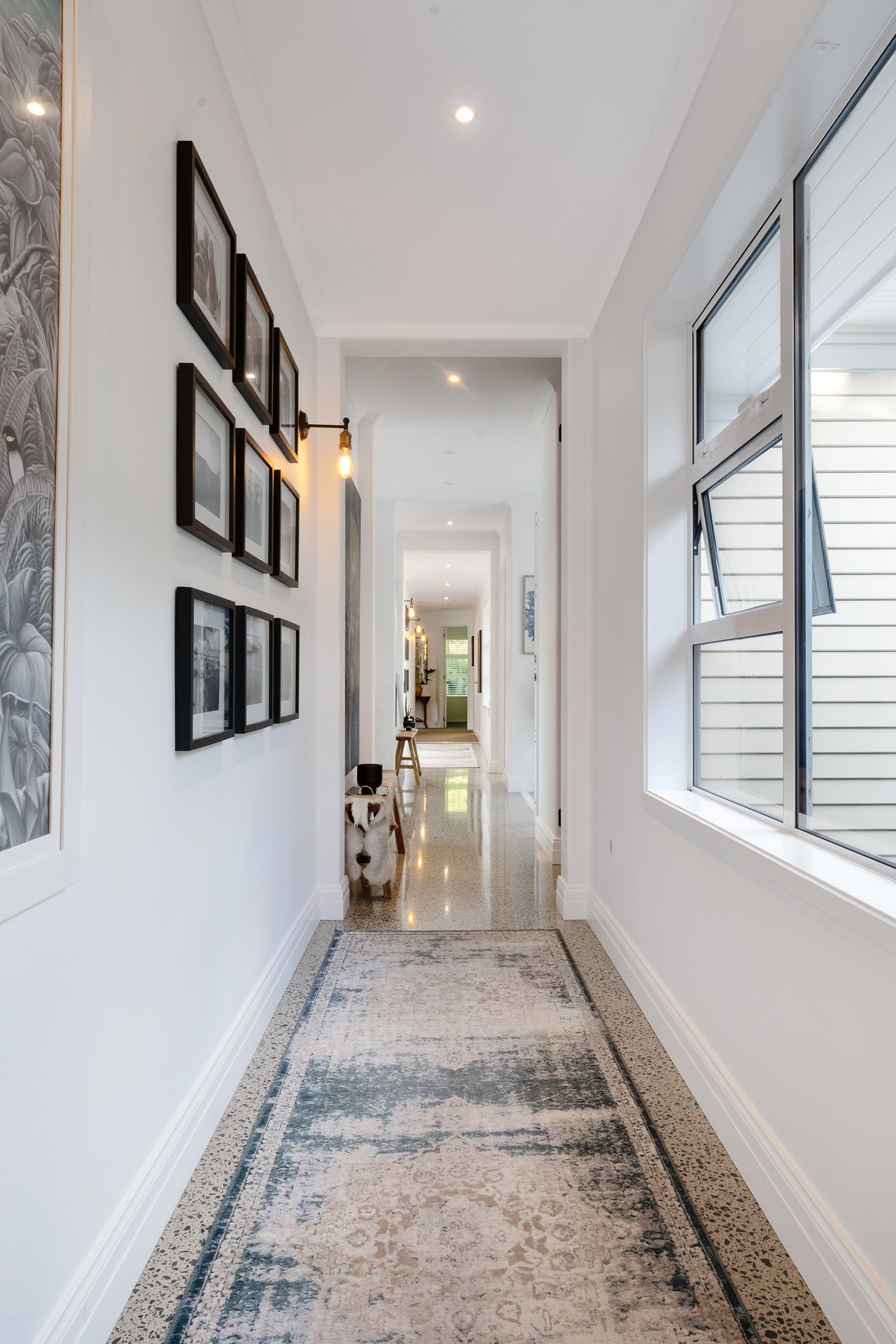 Long white hallway with framed artwork, runner rug, and modern wall sconces.