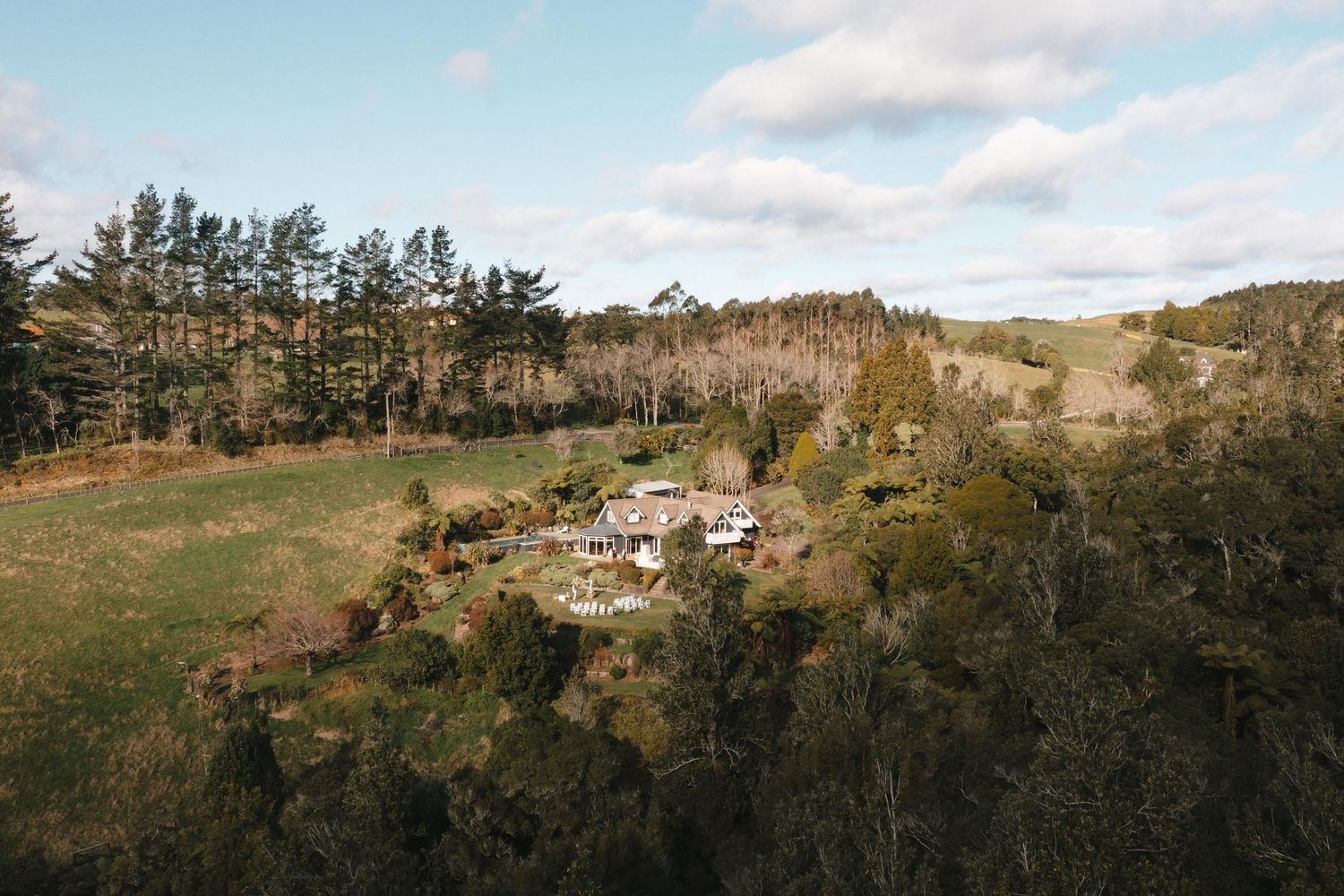 Aerial view of a small rural settlement nestled among rolling hills and pine trees in a scenic countryside landscape.