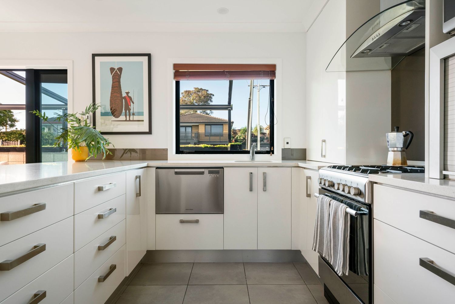 Minimalist white kitchen with sleek cabinets and natural light flowing through multiple windows.