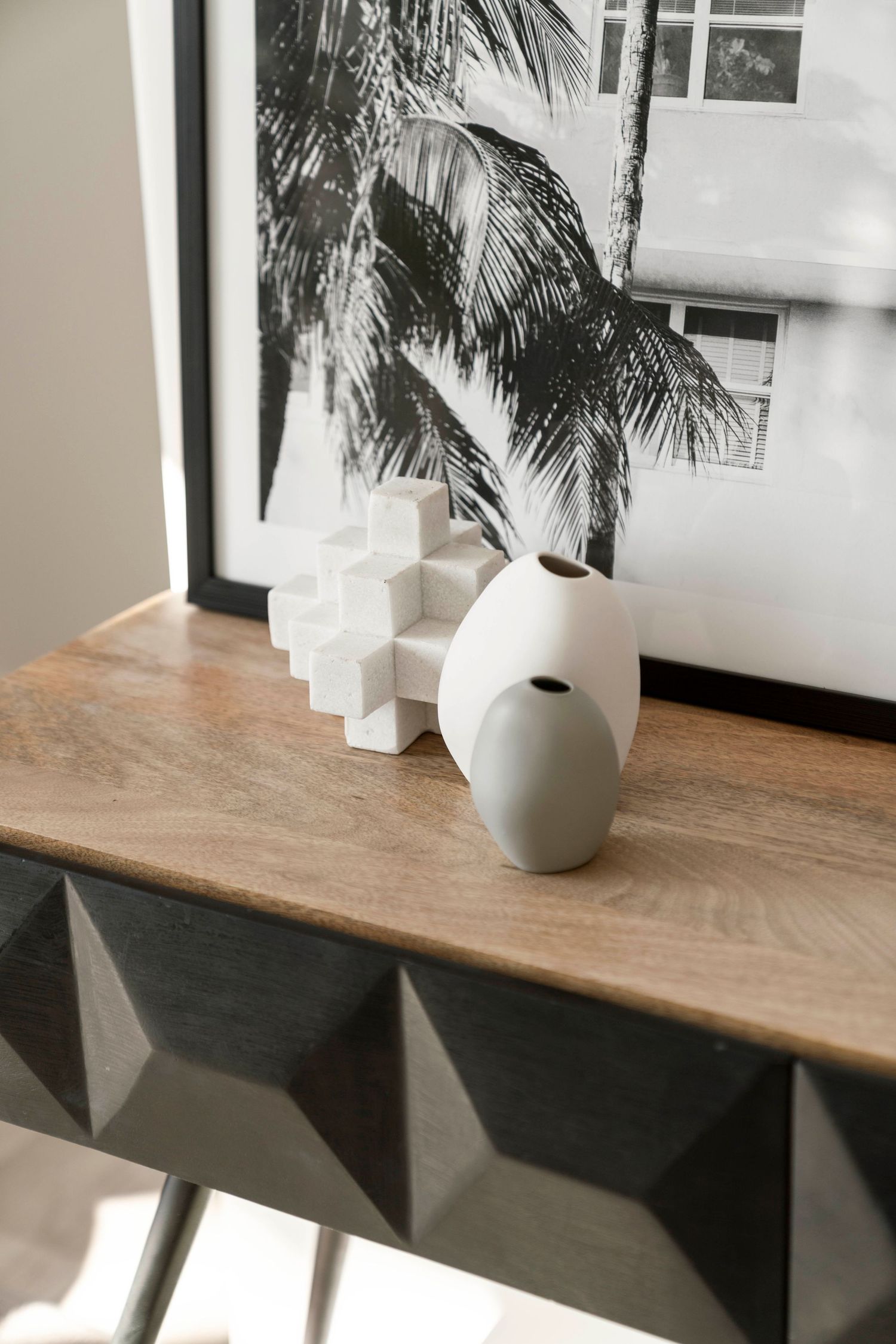 Minimalist wooden table display with a white ceramic vase in natural sunlight.