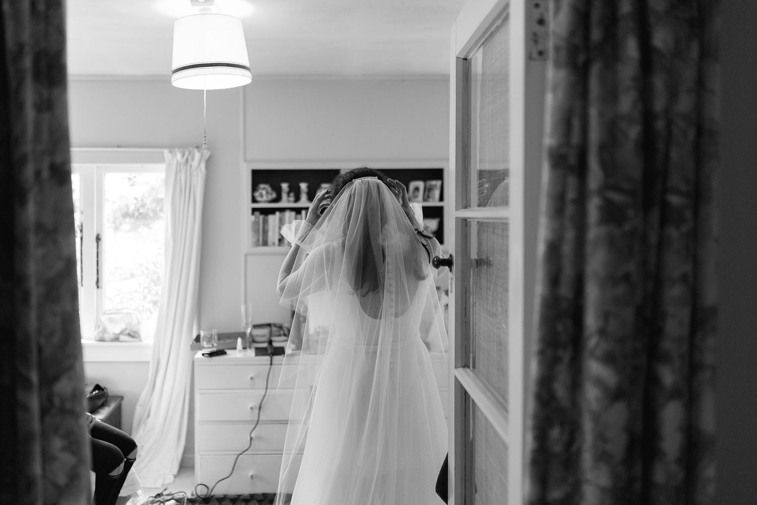 A figure in a wedding veil is photographed from behind in black and white as they prepare for their special day.
