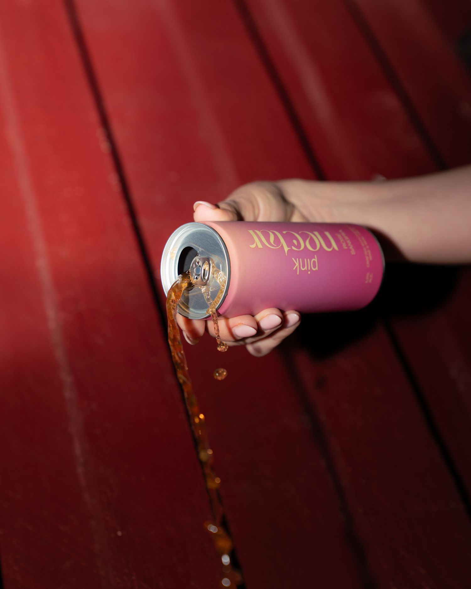 Nectar beverage being poured from pink can showing liquid stream with sparkles.