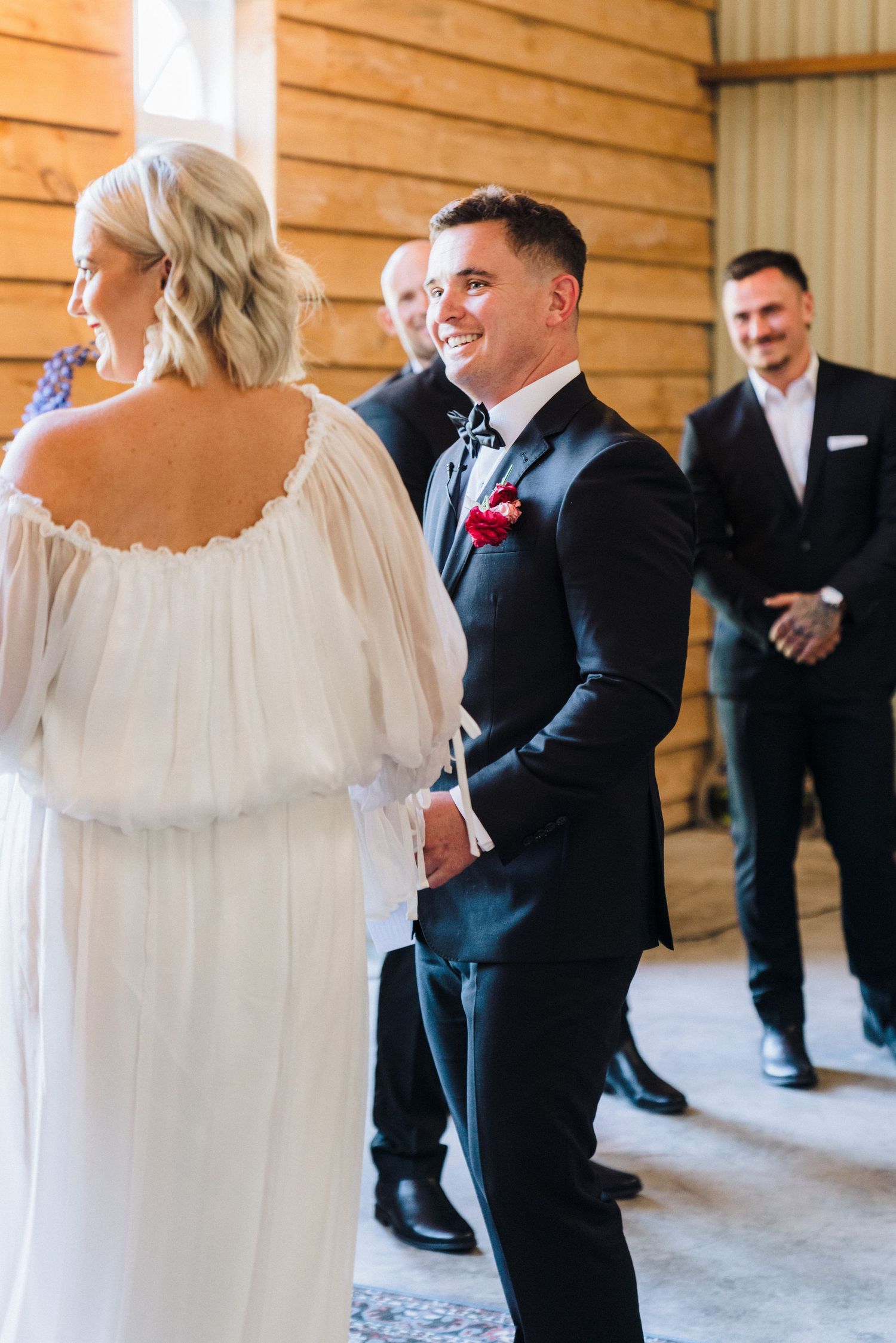Wedding party members in formal black and white attire gather together in a rustic wooden venue.