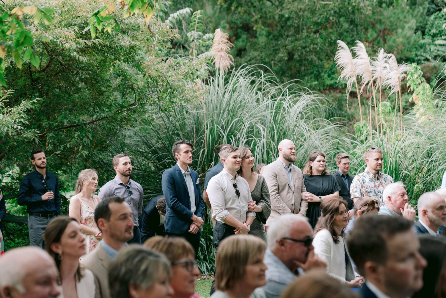 Wedding guests seated outdoors during garden ceremony surrounded by natural landscaping.