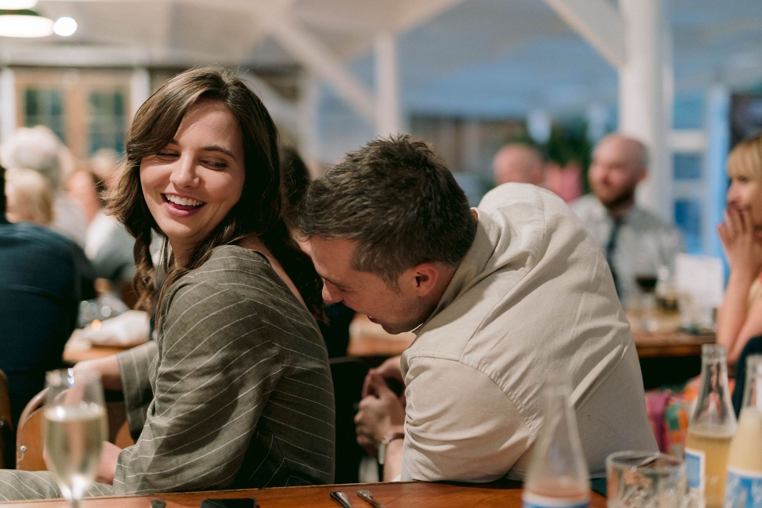 Wedding guests share a candid moment at a reception table with warm indoor lighting.