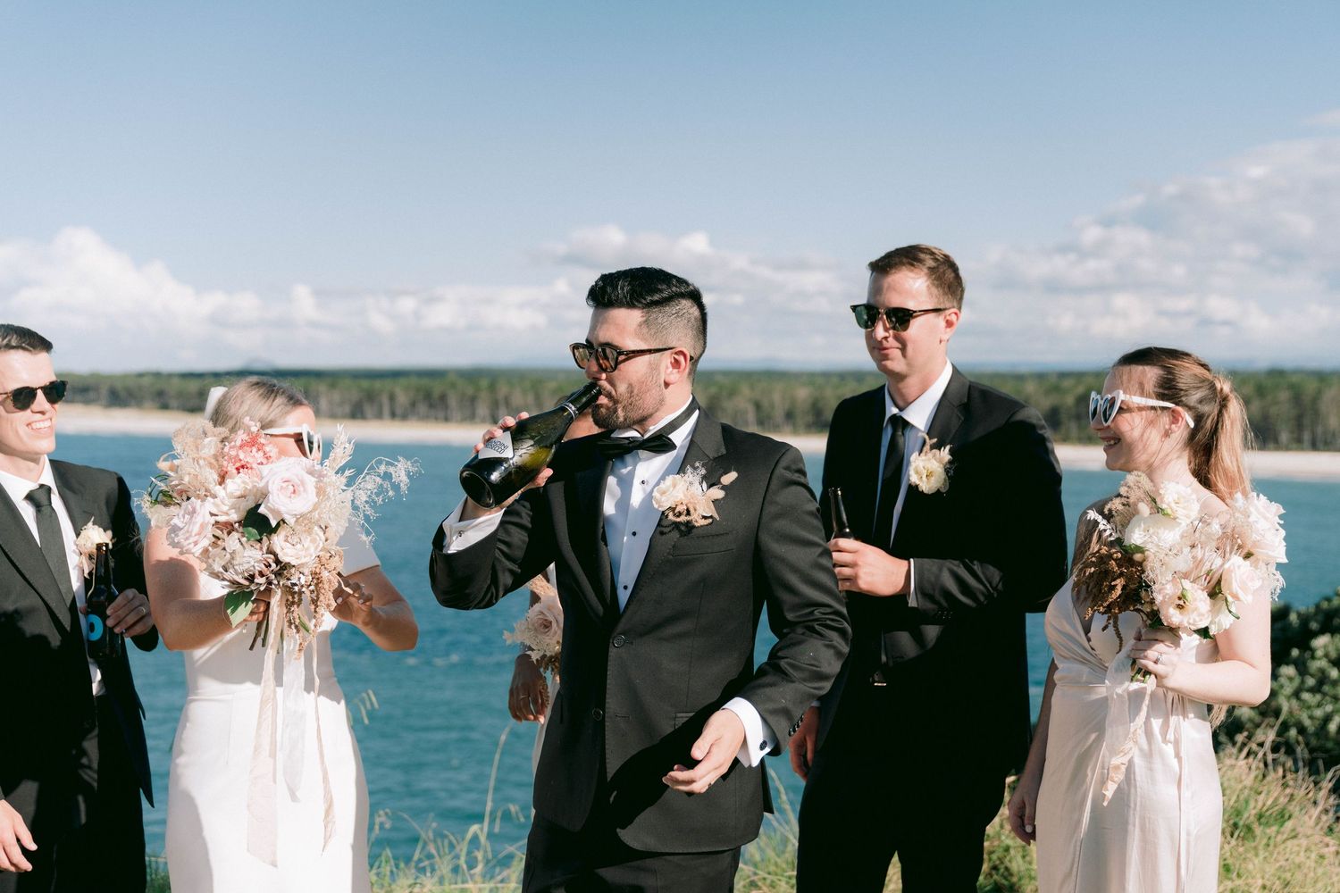 Wedding party members celebrate and toast during outdoor waterfront photo session.
