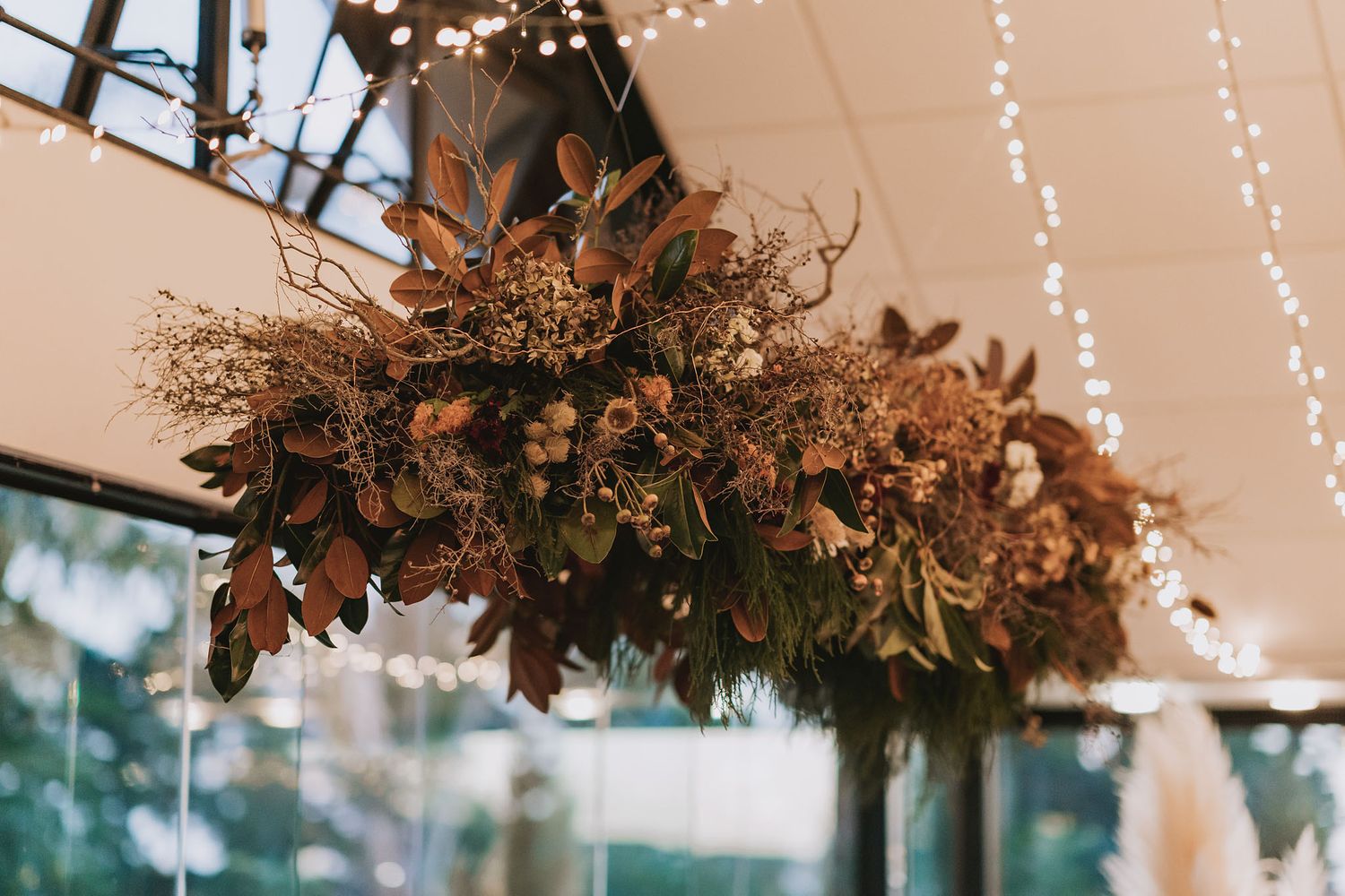Cozy rustic wedding reception venue decorated with twinkling string lights and natural greenery garlands overhead.