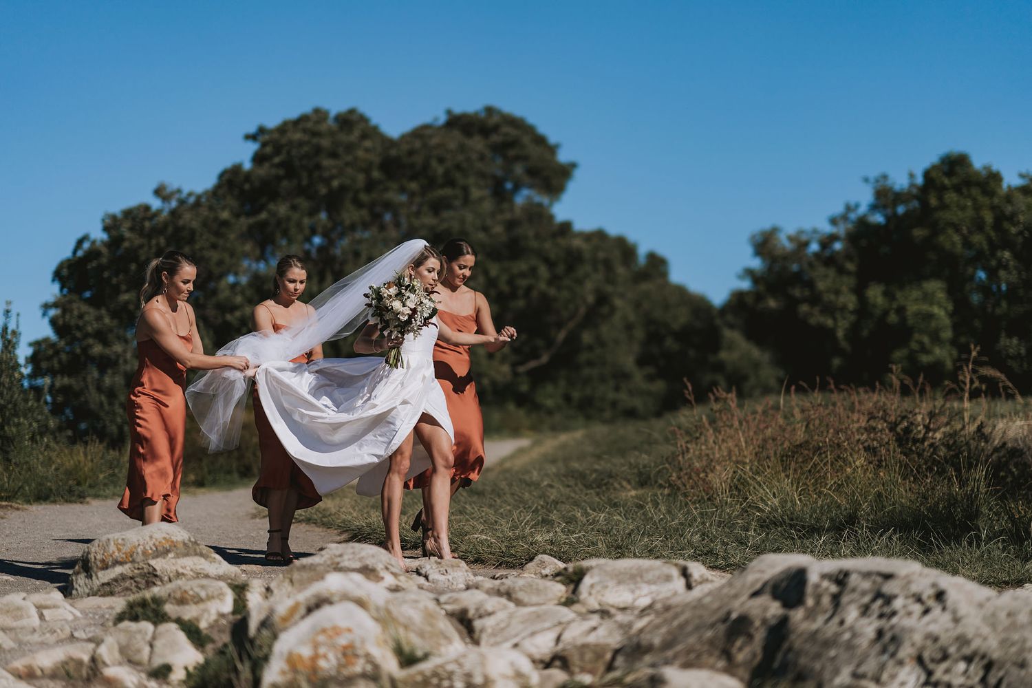 Wedding party having fun capturing candid moments outdoors on stone wall with flowy white dress.