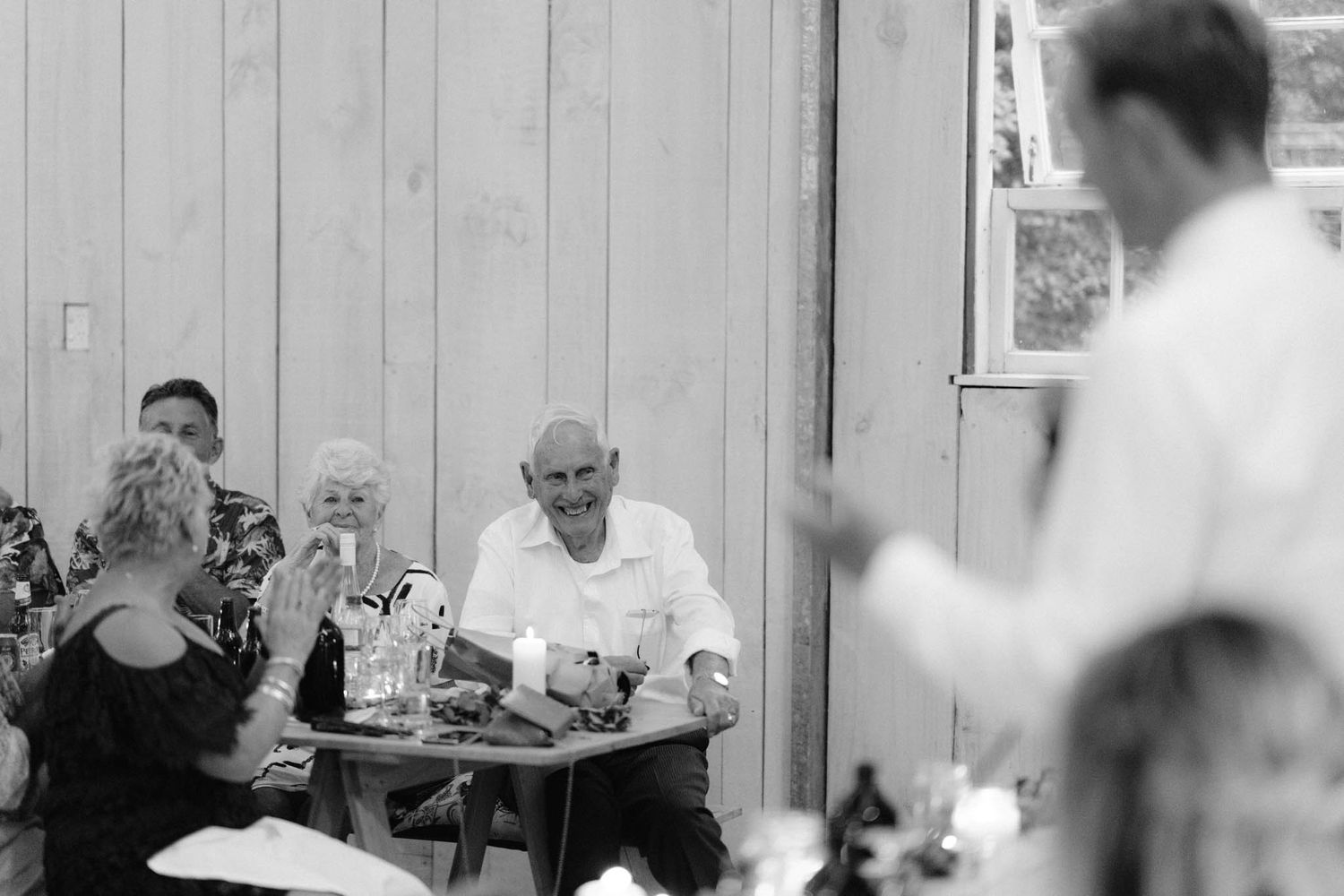 Black and white photo showing people seated in a dining room with drinks and refreshments on the table.