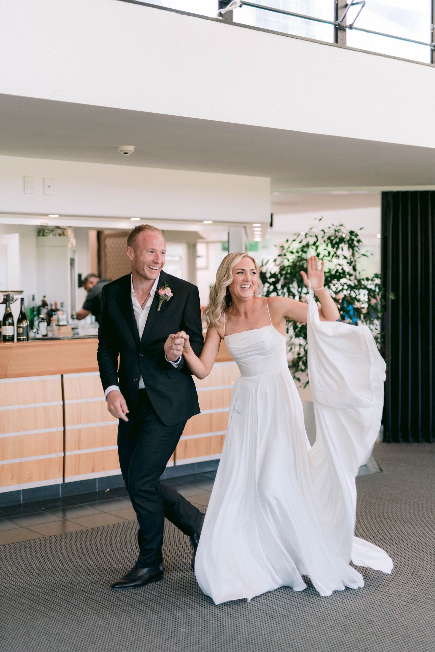 A couple in formal attire dancing playfully inside an indoor venue during their wedding celebration.