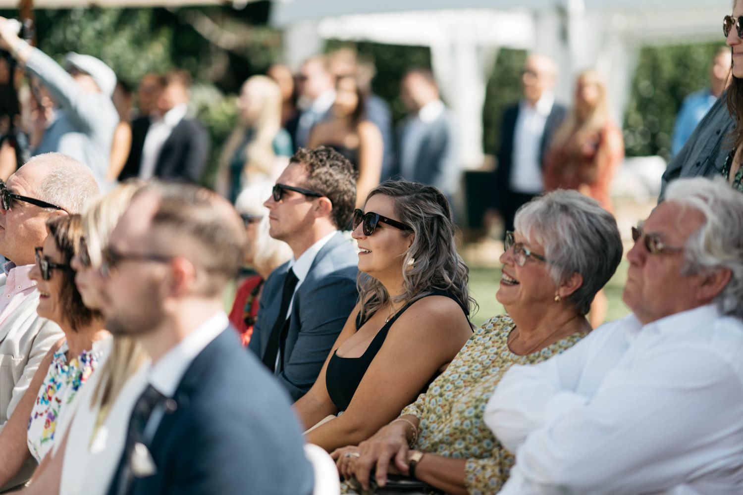 Wedding guests sitting outdoors at a ceremony looking upward in focus and anticipation.