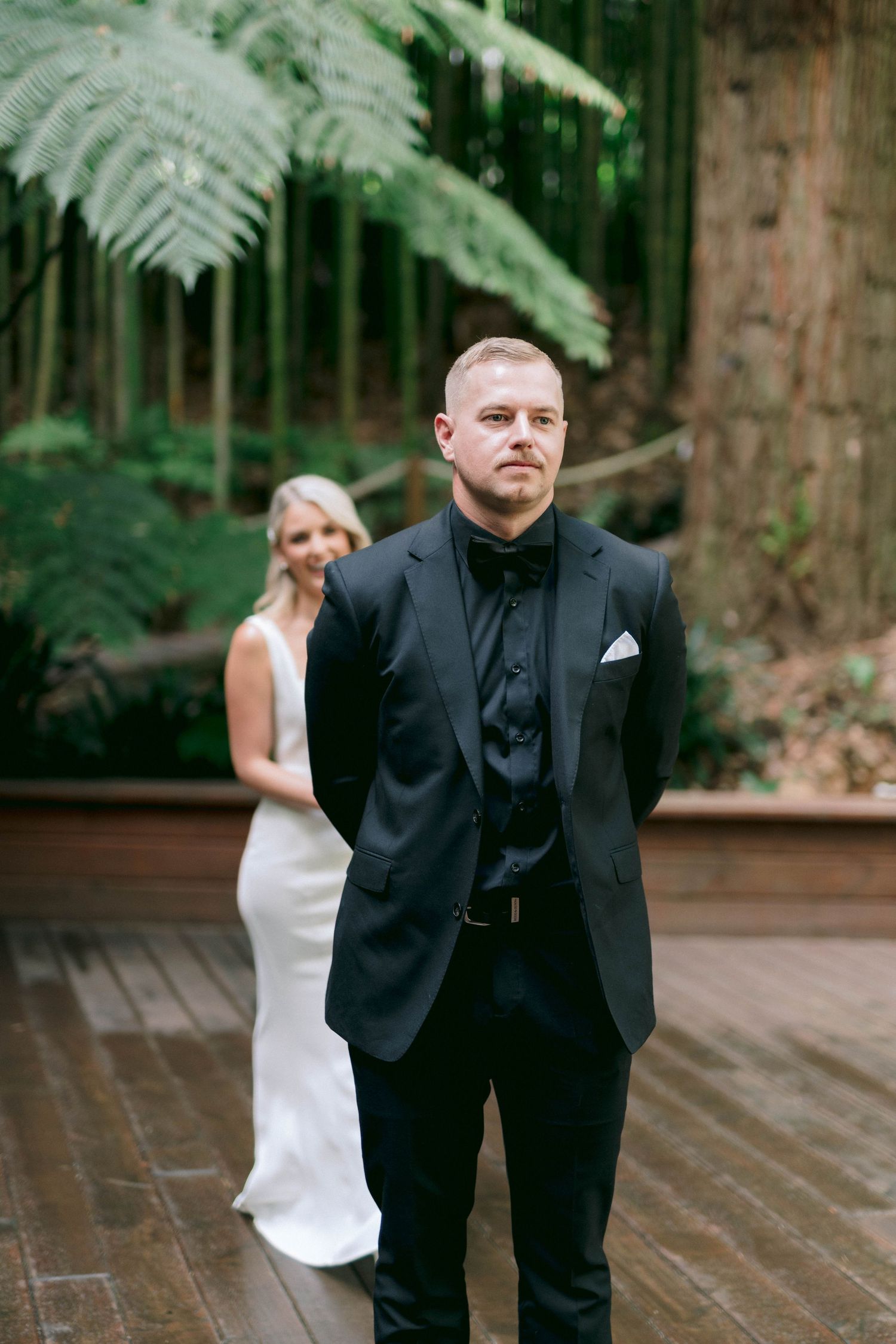 A couple shares a first look moment in a lush forest setting with ferns.