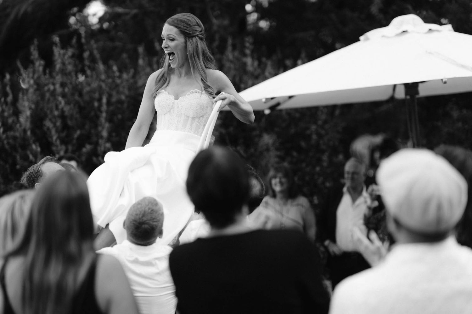 A black and white wedding scene of a couple dancing outdoors under white umbrellas at an elegant celebration.