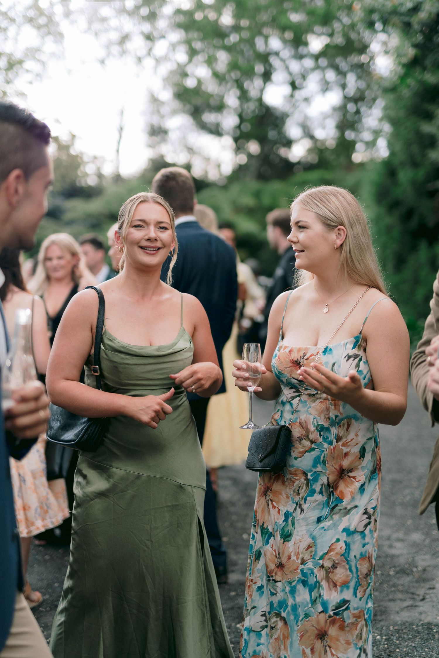 Two guests engage in lively conversation at an outdoor social gathering, with one wearing olive green attire.