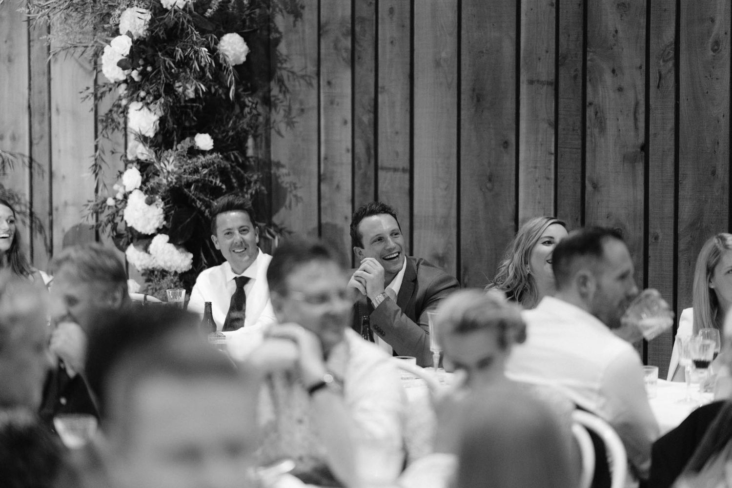 Black and white photo of wedding guests seated at outdoor reception tables with string lights overhead.