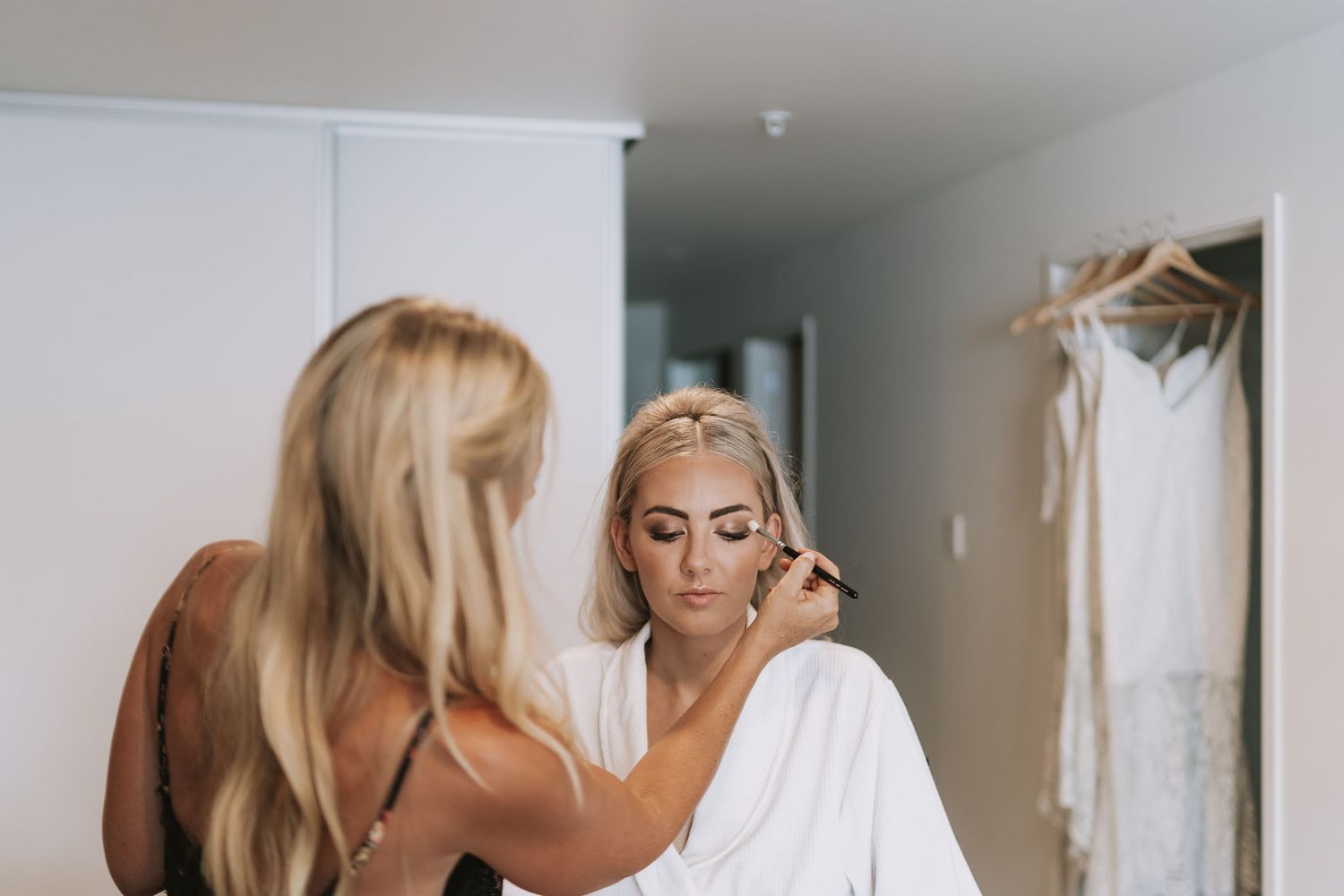 Wedding preparations show a person getting hair and makeup done in a white robe while someone assists.