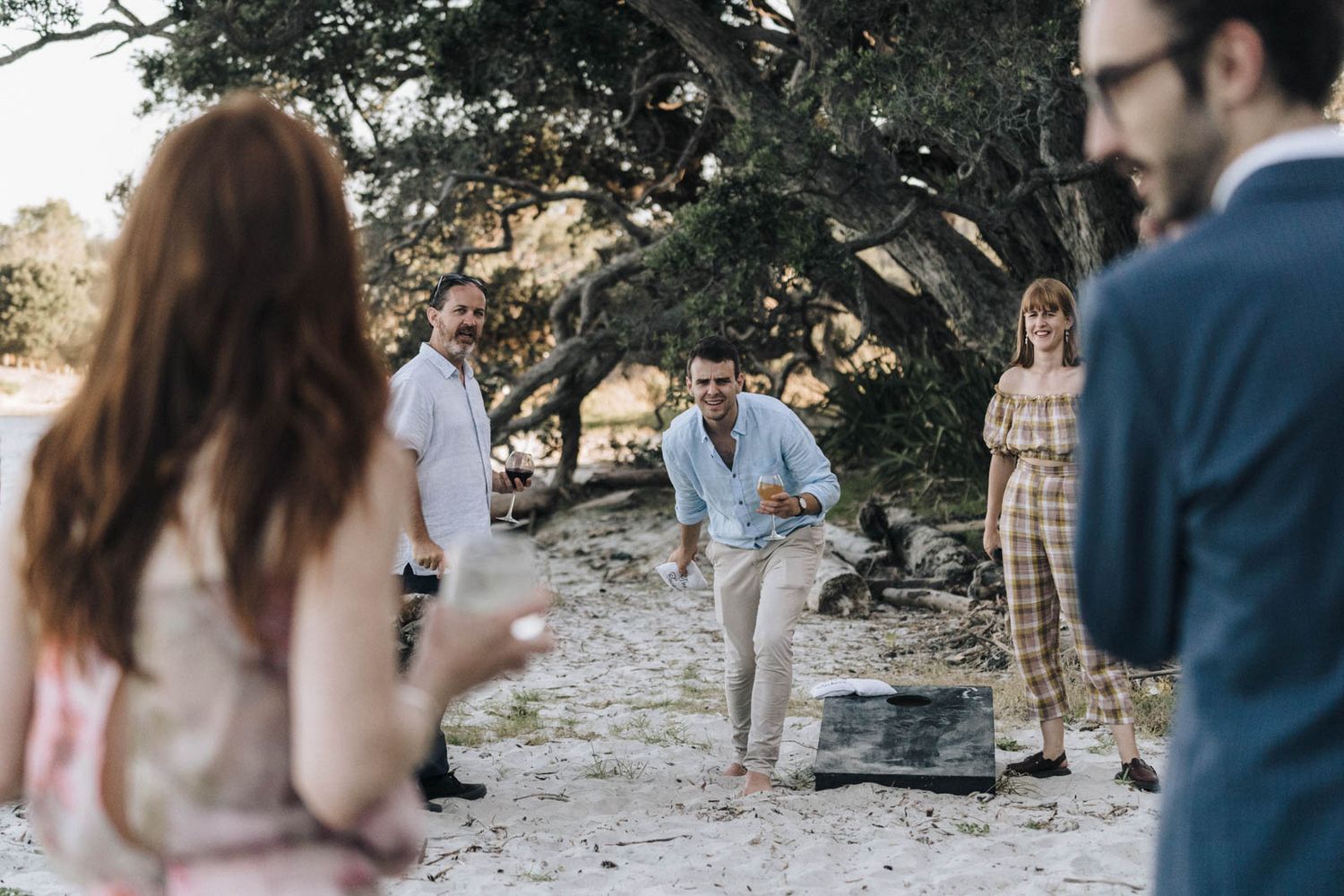 Guests gather outdoors on a rugged terrain path with trees in the background during a casual event.