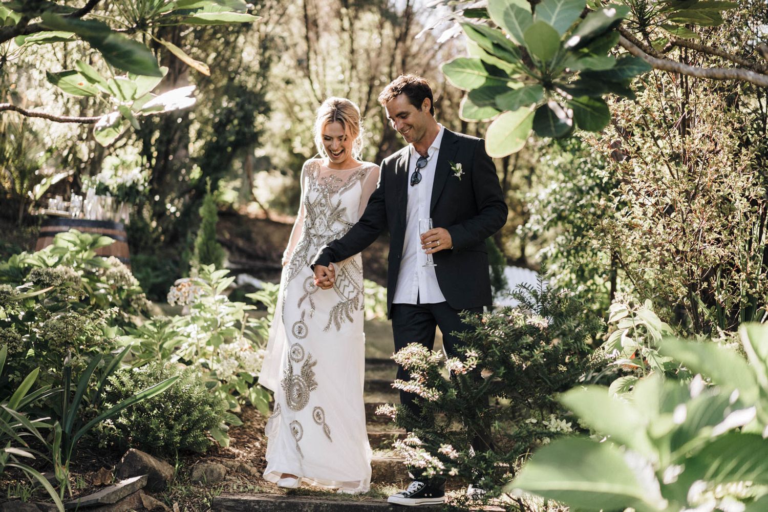A romantic wedding couple poses on stone steps in a lush tropical garden setting.