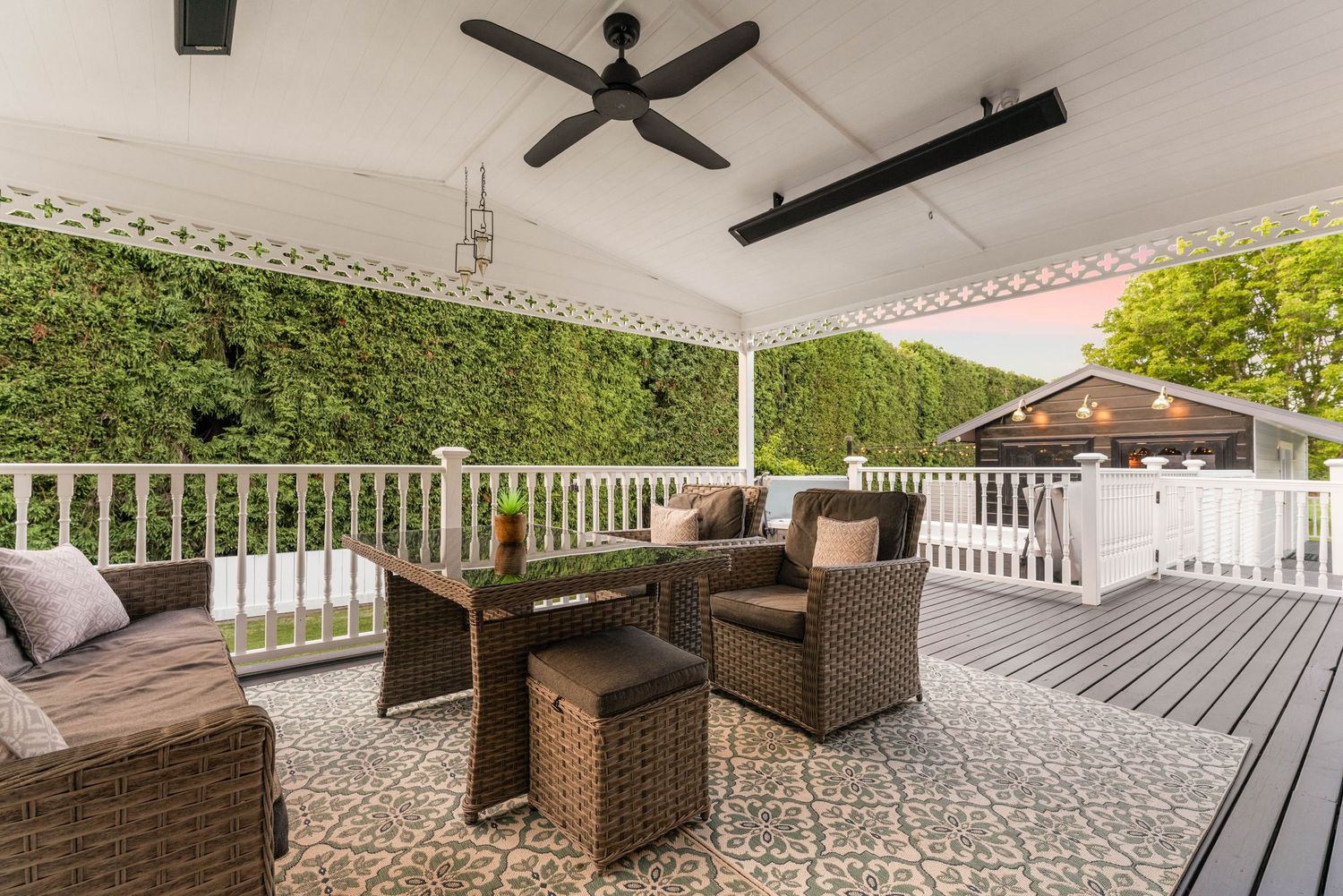 Cozy covered patio with wicker furniture and decorative pattern tiles surrounded by green hedge walls.
