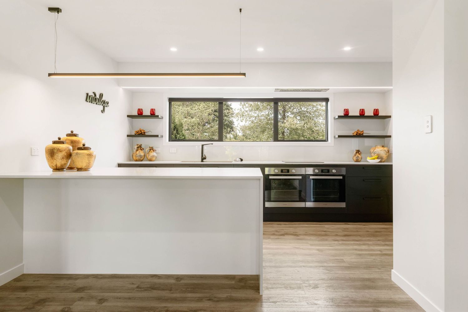 Minimalist white kitchen interior with long countertop and floating shelves.