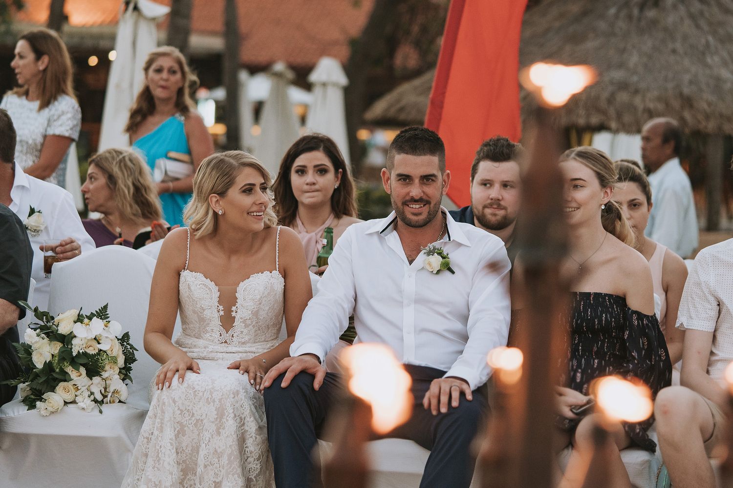 A wedding ceremony at sunset showing guests seated outdoors with elegant white floral arrangements.