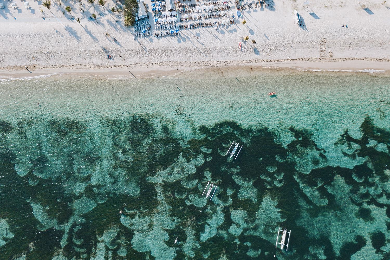 Aerial view shows turquoise ocean waters meeting sandy beaches along a rocky coastline.