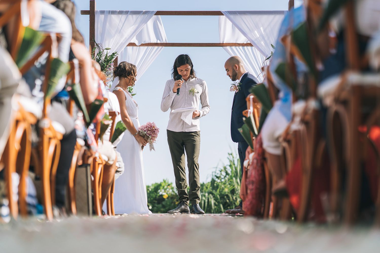 Guests watch as participants walk along wooden deck during outdoor ceremony.