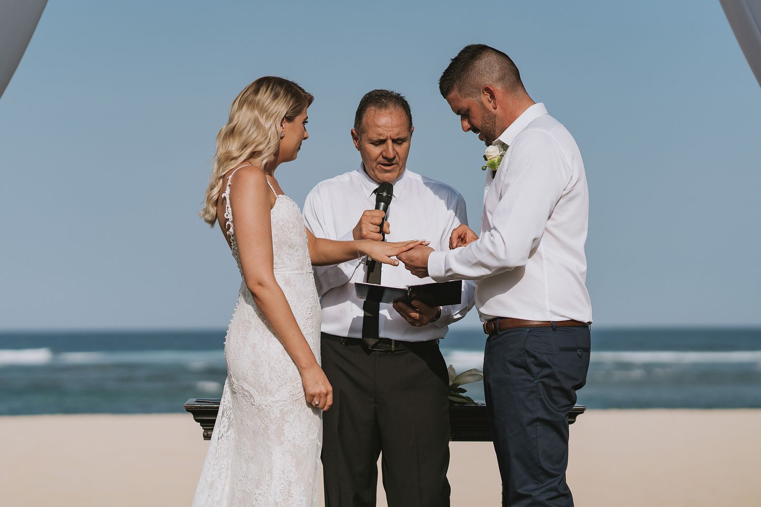 Beachside wedding ceremony with couple and officiant against ocean backdrop.