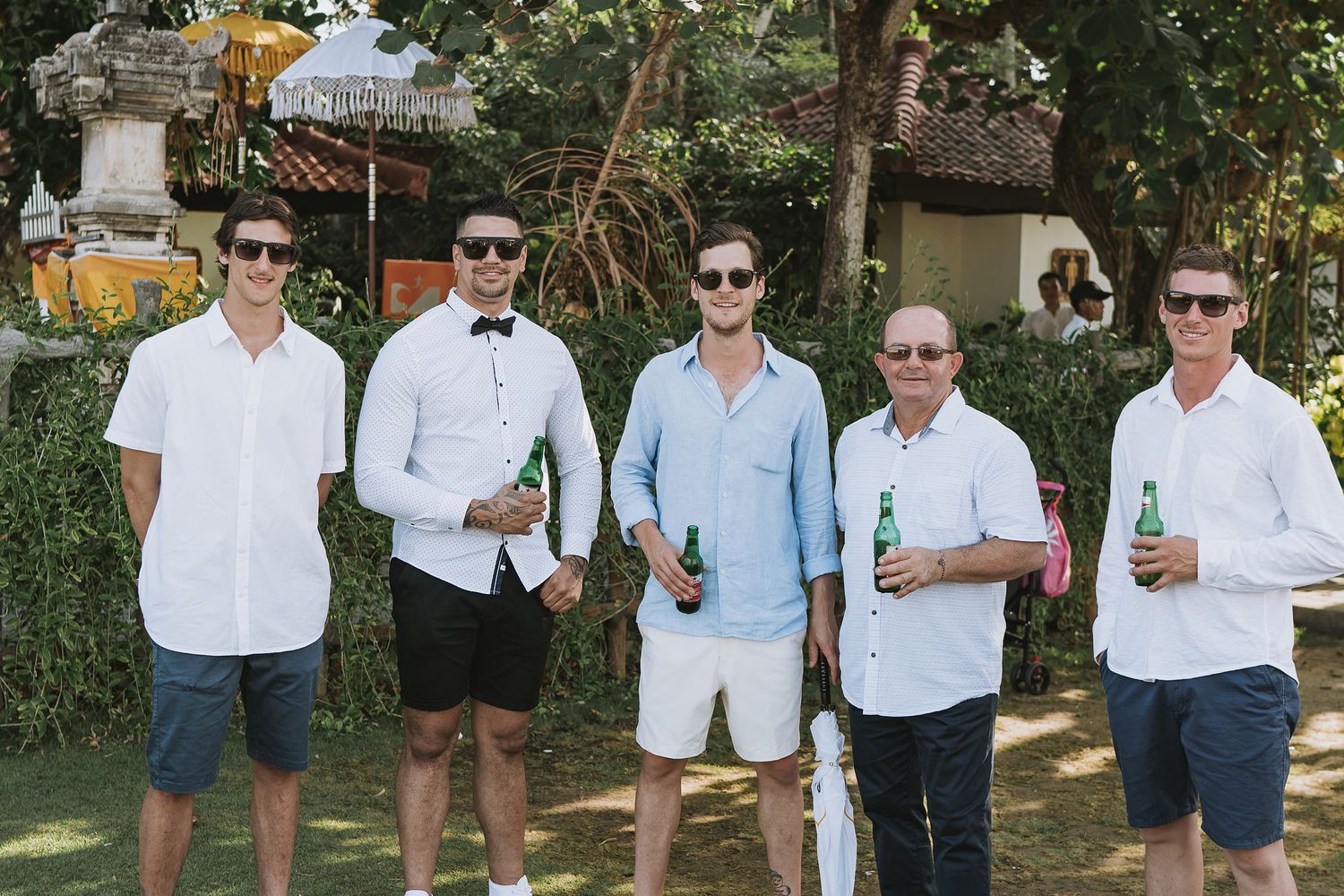 Group of friends in casual summer attire holding drinks at an outdoor gathering.