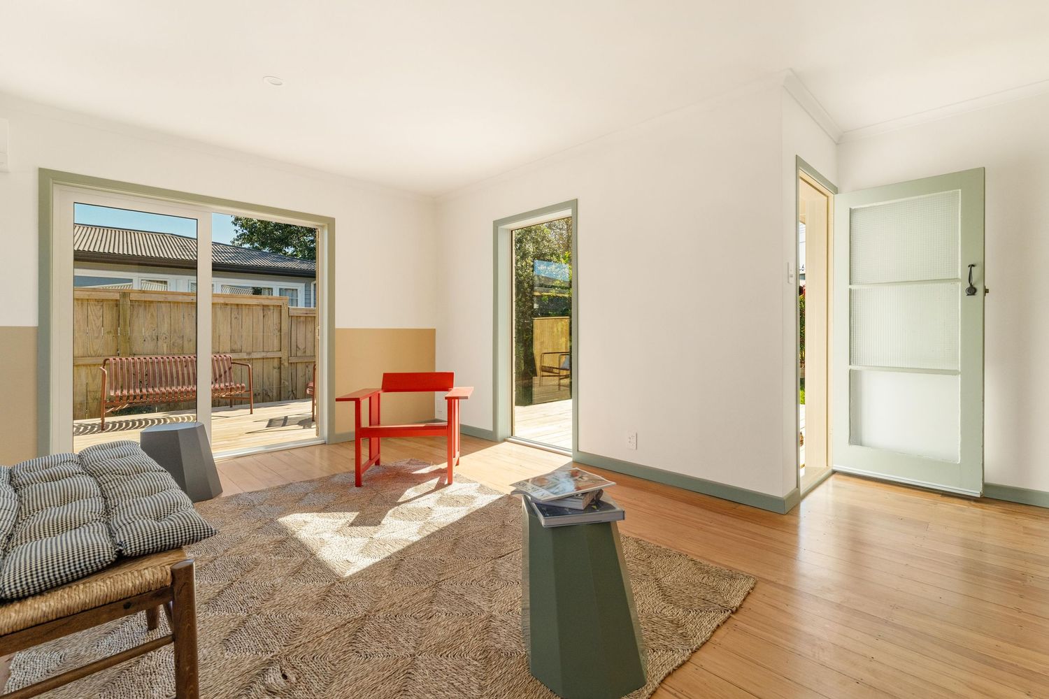 Modern living room with gray sofa, orange chair, and wood flooring features large window overlooking fenced backyard.