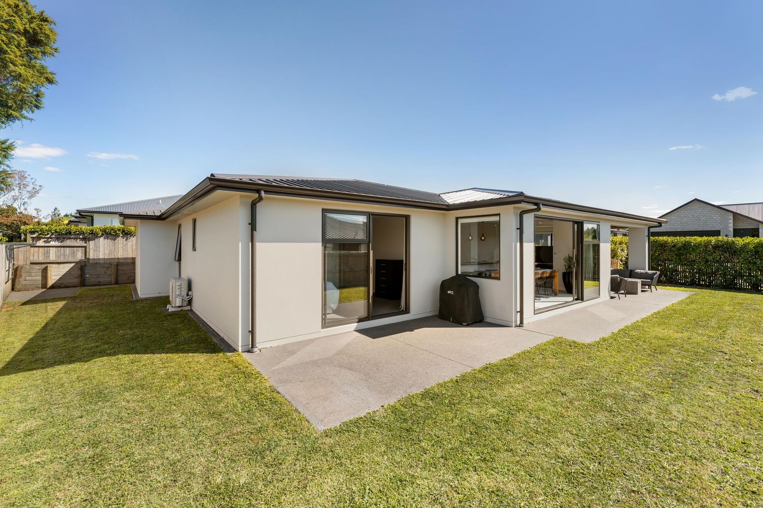 Contemporary single-story home with white exterior walls and large windows featuring a well-maintained lawn and concrete patio.