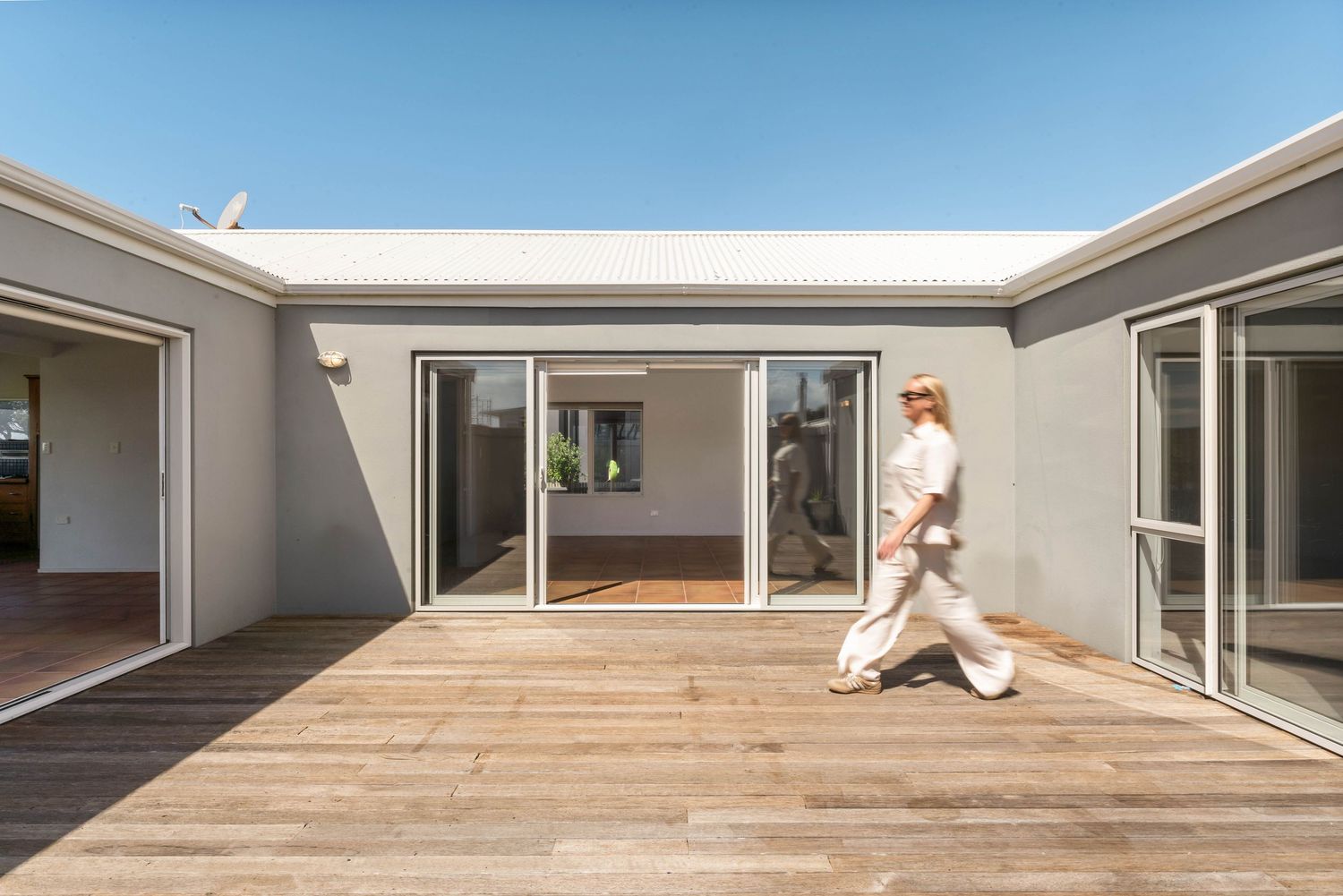 Modern home exterior featuring a wooden deck patio with glass sliding doors and minimalist architecture.