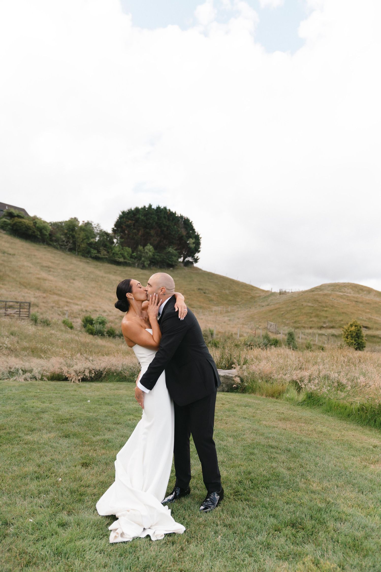 A couple in wedding attire share a romantic moment in a scenic hillside setting.