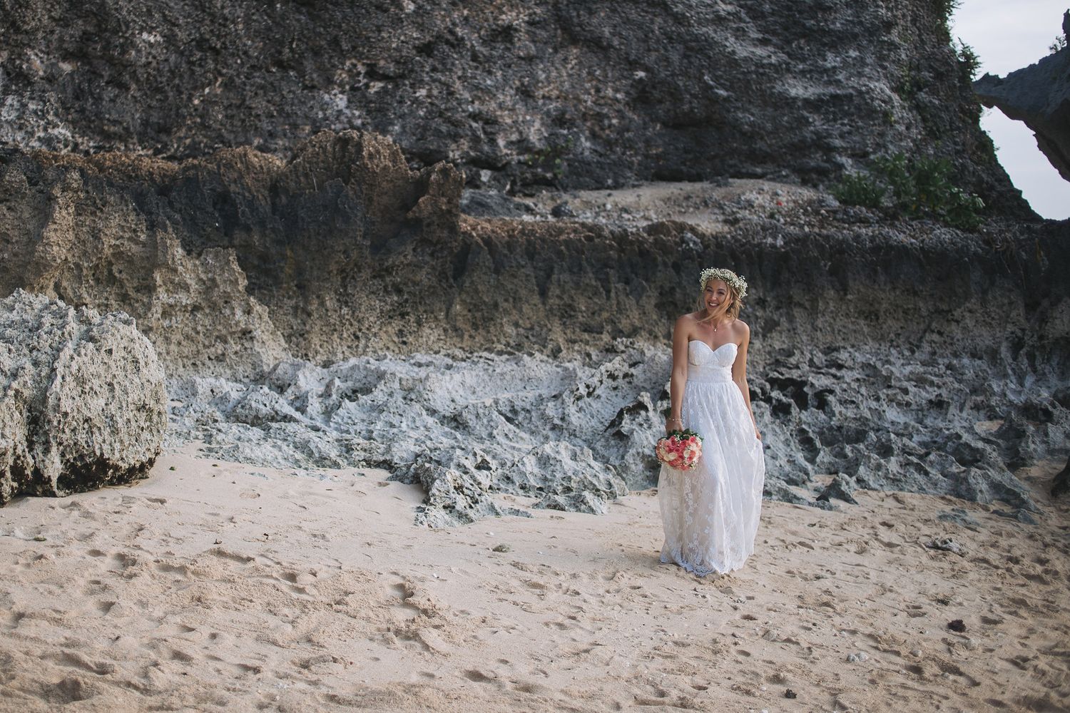 Person in white dress walking along scenic beach cliffside during outdoor photoshoot session.