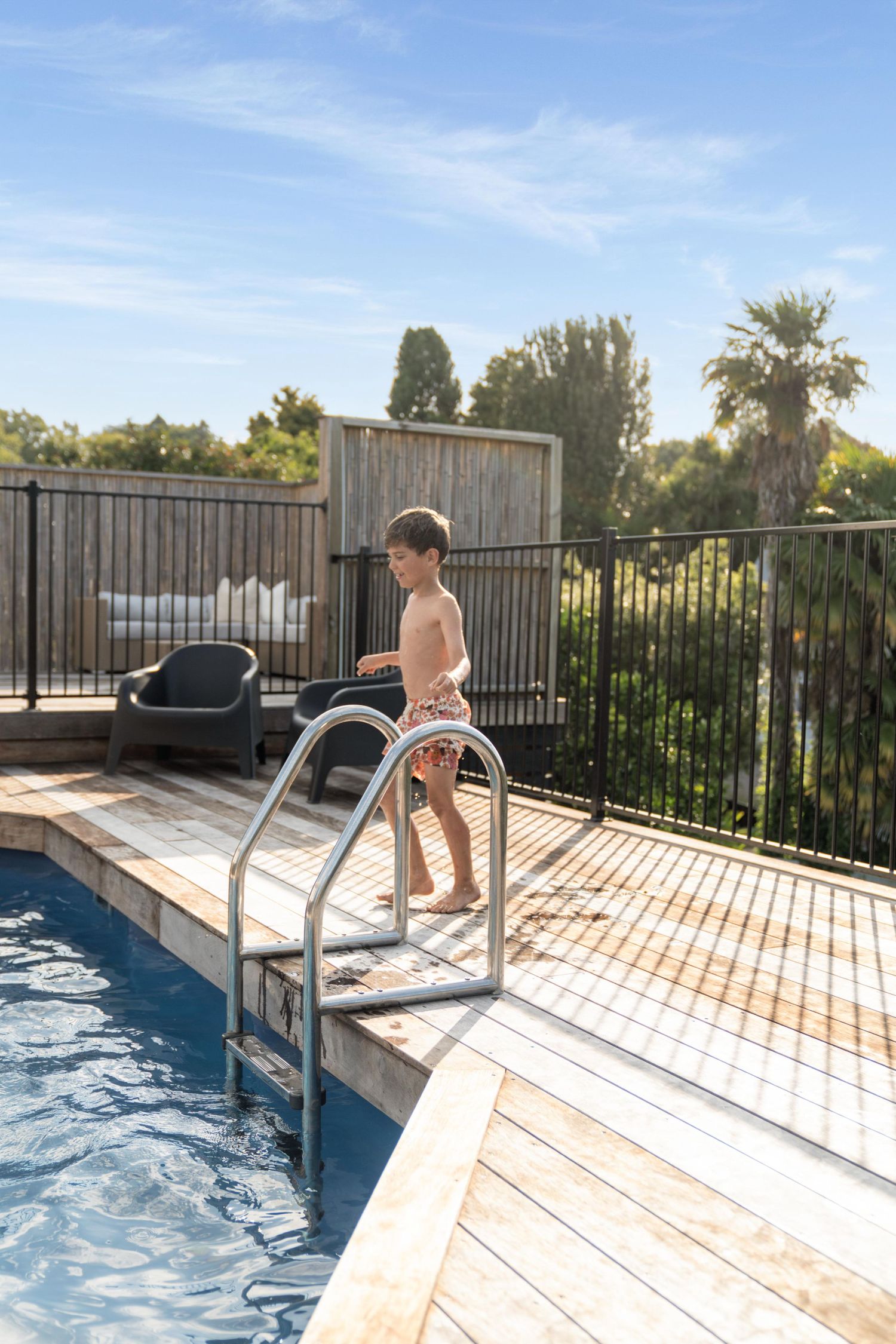 Swimming pool with wooden deck and safety railing against a blue sky backdrop.