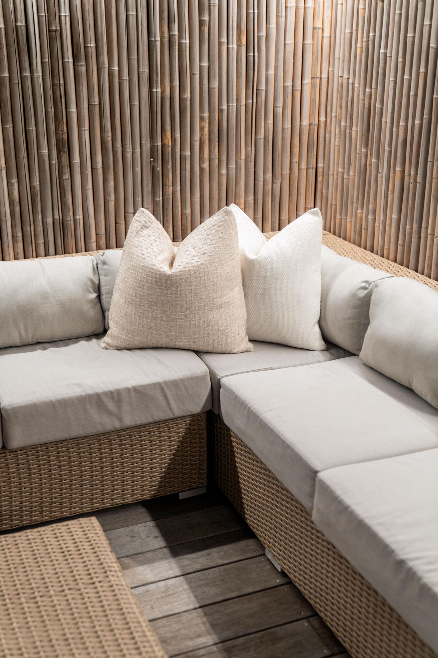 Outdoor lounge area with wicker furniture and plush white cushions against bamboo privacy screen.